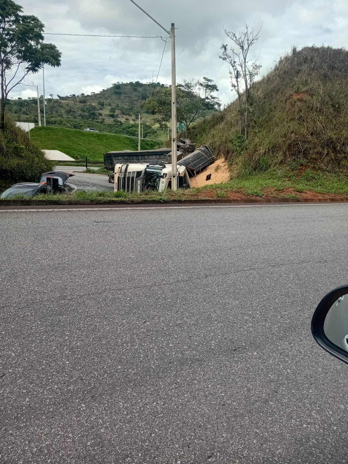 Vista da rodovia: a carreta tombada na alça do trevo, com a soja espalhada junto ao barranco. Foto: Redação Rádio Cultura
