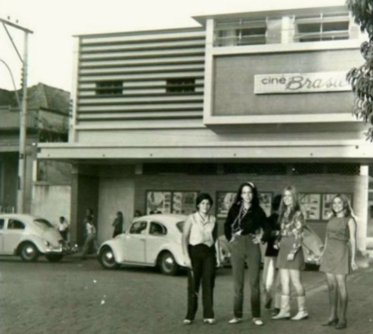 Moças diante da fachada do Cine Brasil, com os Fuscas estacionados na Praça Dr. Augusto Silva