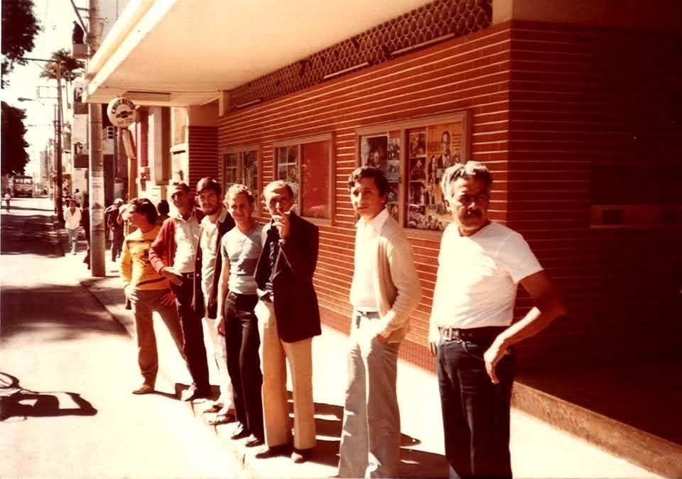 A família Torquetti na calçada do Cine Brasil, com os cartazes dos filmes em cartaz expostos na parede de tijolinho