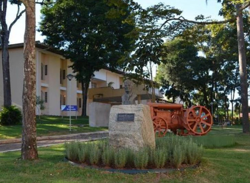 Trator antigo exposto ao lado de um busto, no câmpus da UFLA · Foto: Acervo Memórias UFLA/Reprodução